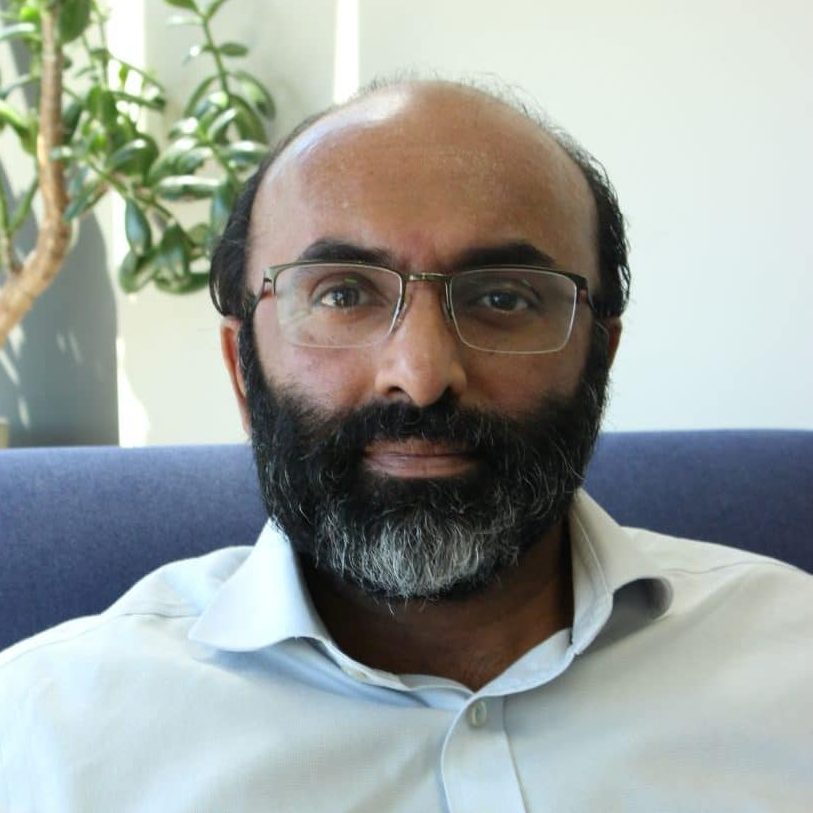 Dr Shyam Gangadharan, physician in General Medicine, seated indoors on a blue chair with a plant in the background.