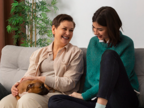 Two adults sitting on a couch with a dog, relaxed home setting